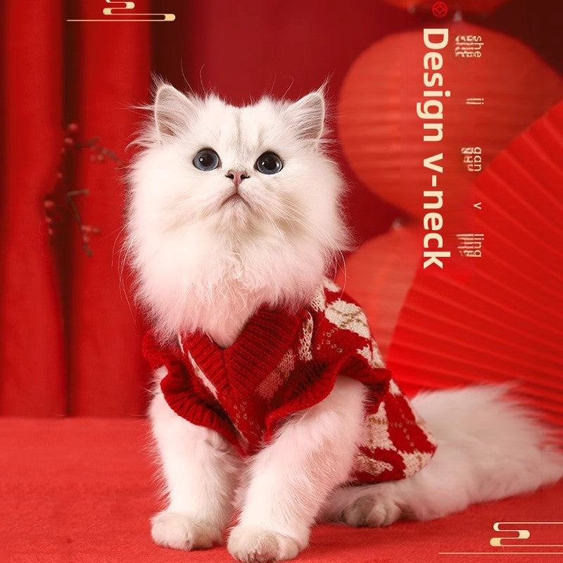 Fluffy white cat wearing a red New Year sweater with v-neck design, surrounded by festive red decor.
