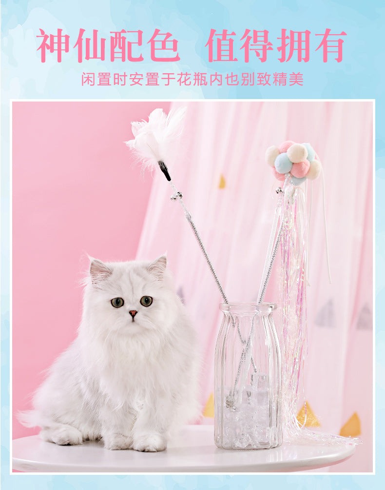 Cat teaser wand toy with feathers and bells in a glass vase, next to a fluffy white cat against a pink background.