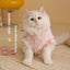 Fluffy white cat wearing a pink winter outfit sitting on a rug.